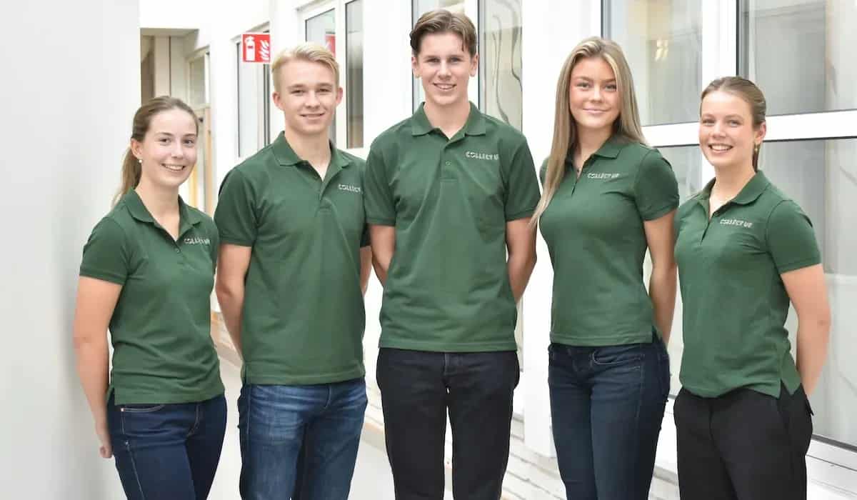 Fem personer i gröna pikétröjor med text står inomhus