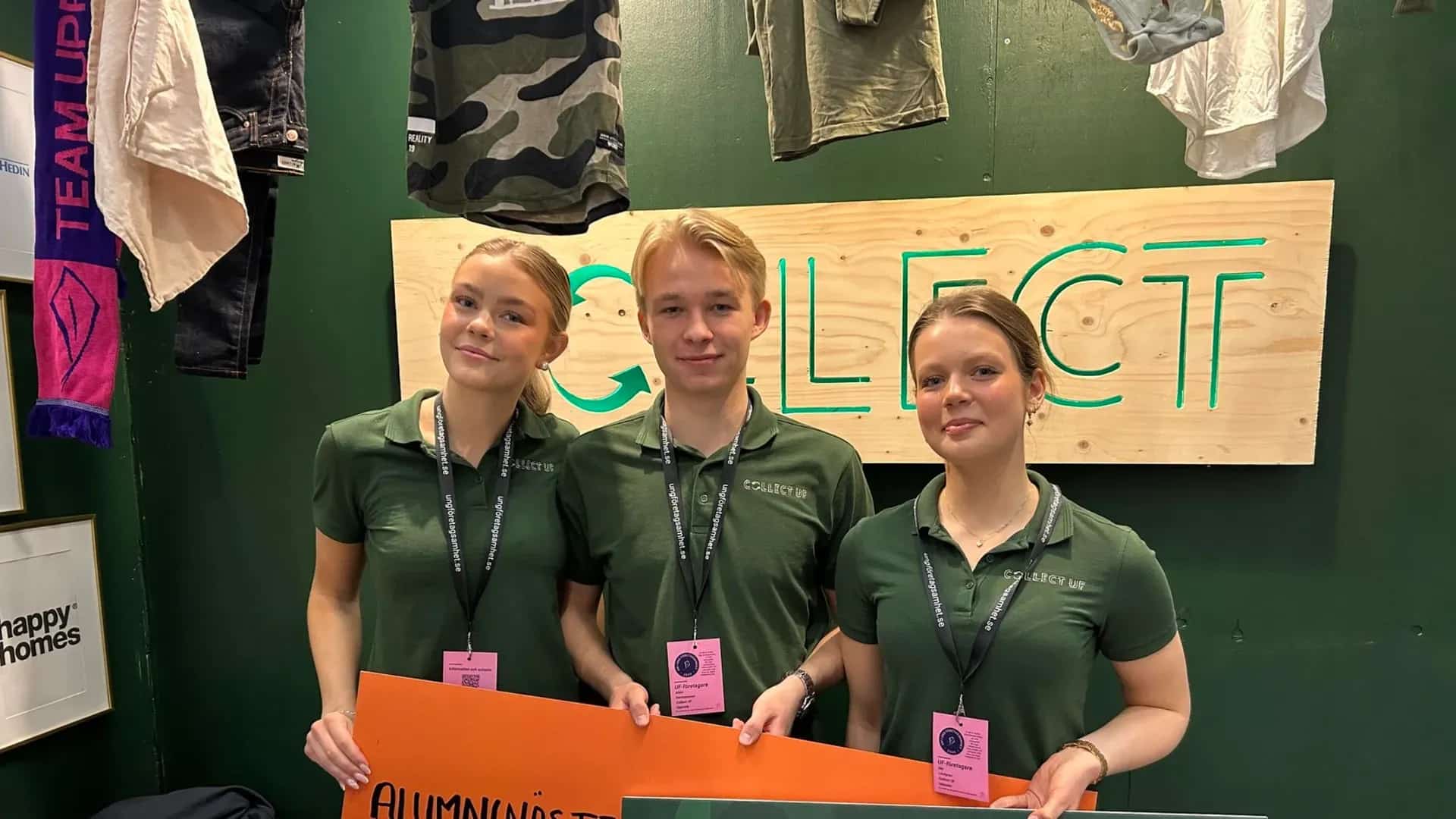 Tre personer i gröna pikétröjor står framför en skylt med texten COLLECT UF. Text på halsband och orange skylt