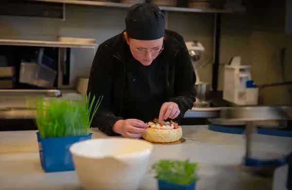 Entré till "Salong 13 Frisör" med rosa blommor i kruka. Grå byggnad i bakgrunden