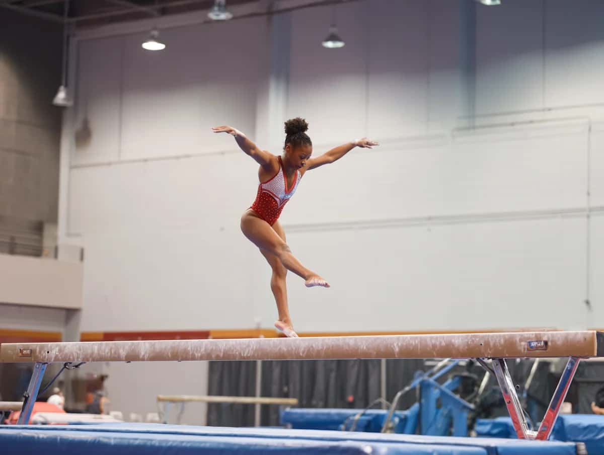 Gymnast i röd och vit dräkt balanserar på en bom med utsträckta armar