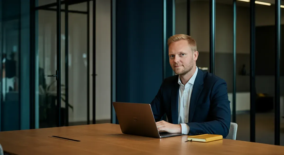 Man ler och gestikulerar. Han lutar mot en stol i ett rum med växter och whiteboard