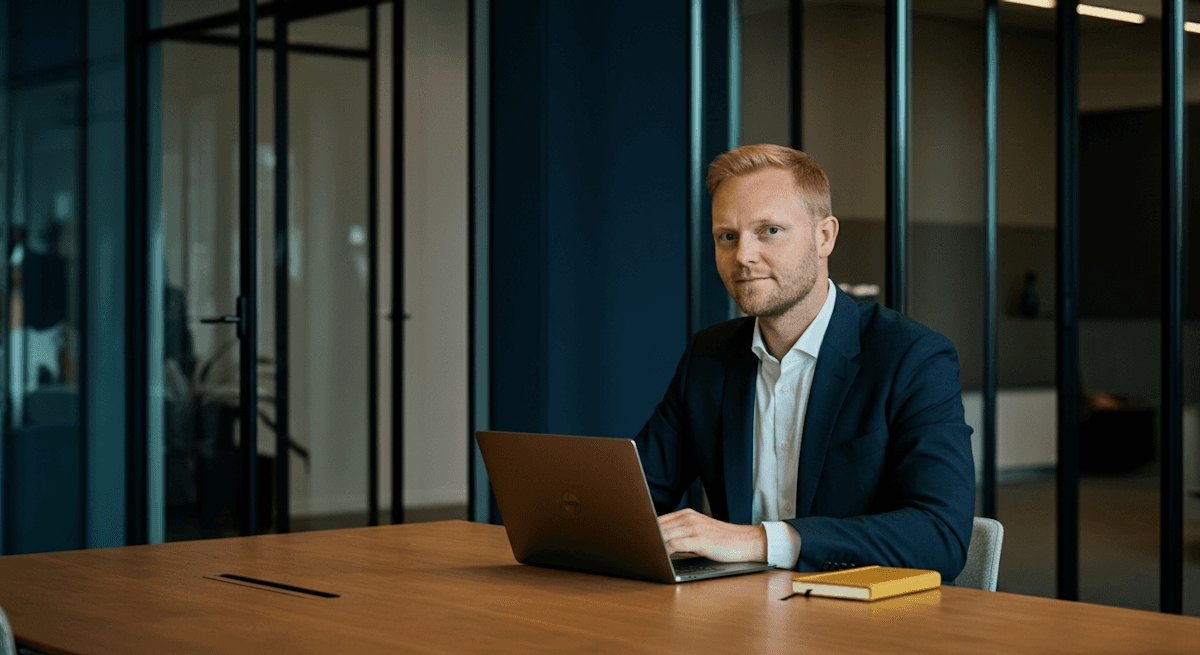 Man ler och gestikulerar. Han lutar mot en stol i ett rum med växter och whiteboard