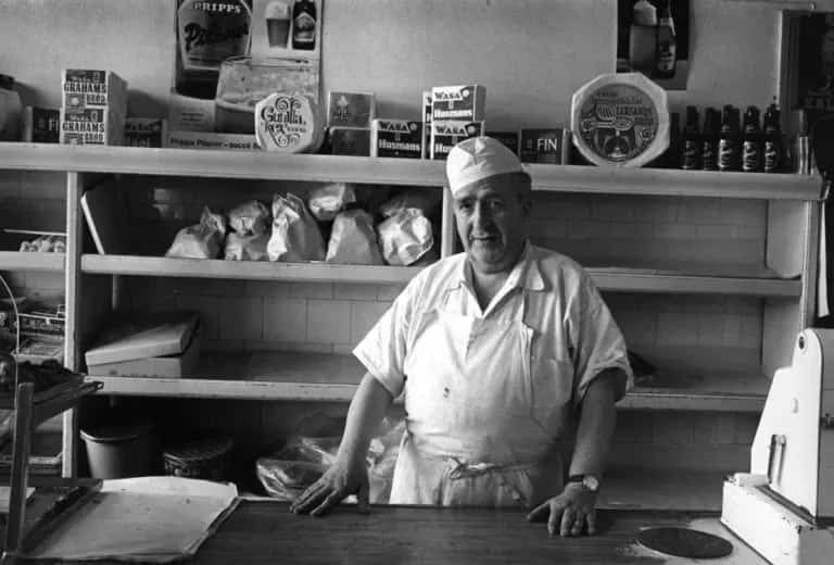 Leende man i grön tröja med text vid vatten, andra människor i förgrunden