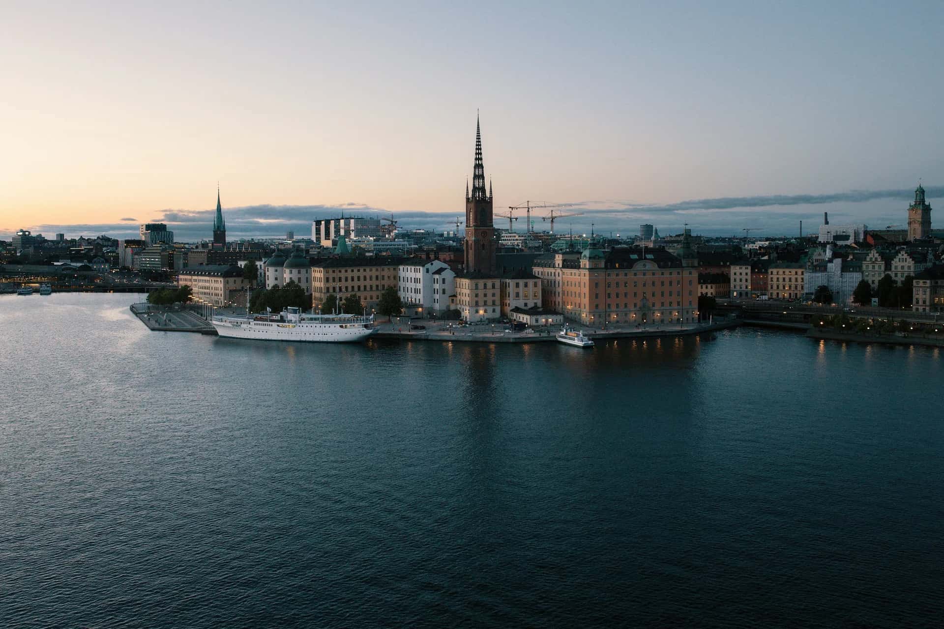 Riddarholmen i Stockholm i skymningsljus med Riddarholmskyrkan och en vit båt vid kajen