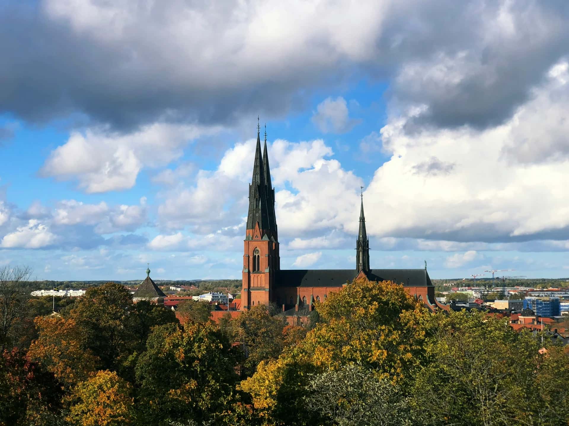 Uppsala domkyrka reser sig bakom höstfärgade träd under en molnig himmel
